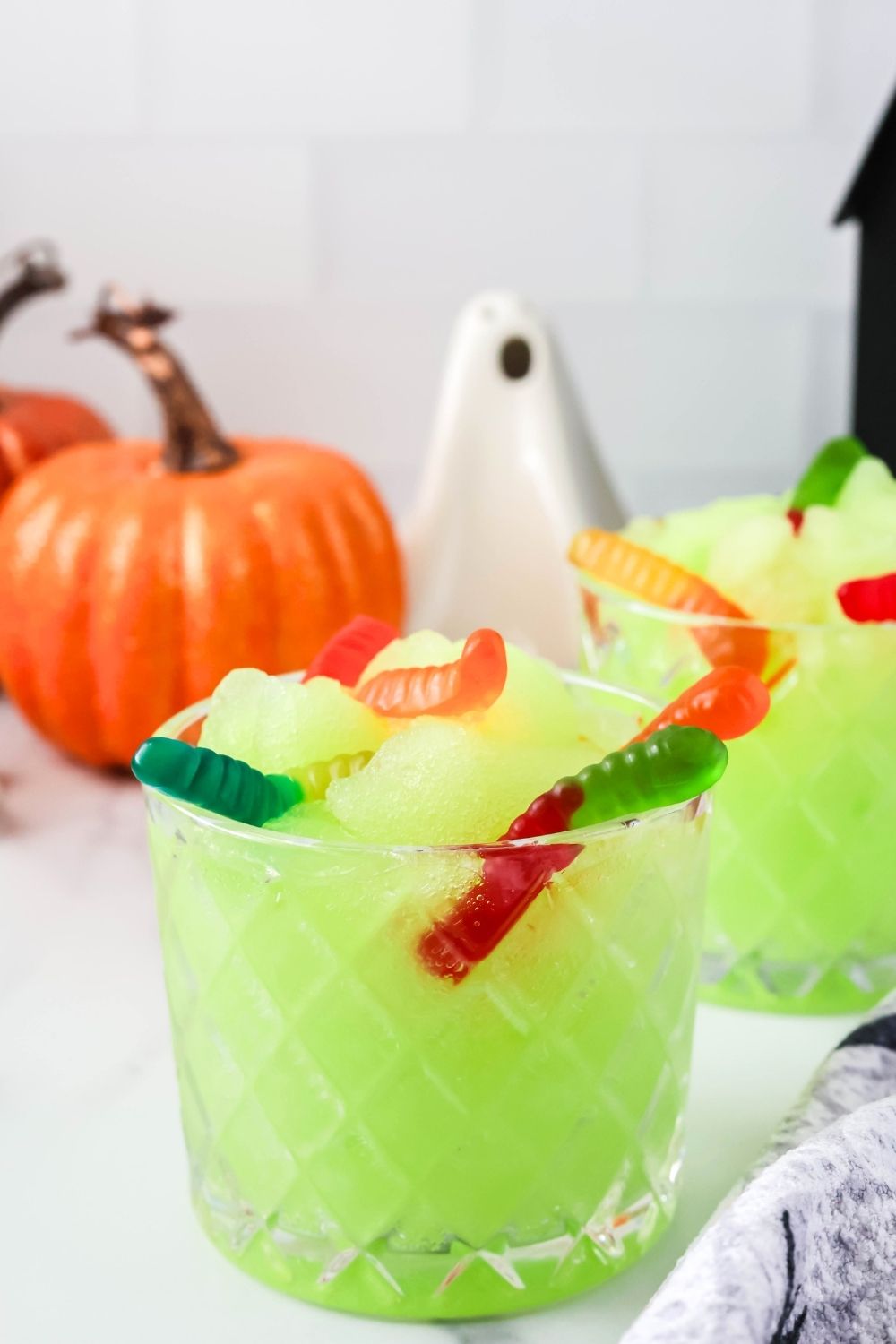 close-up of a glass of kid-friendly green Halloween slush made in the Ninja Slushi machine, garnished with colorful gummy worms.