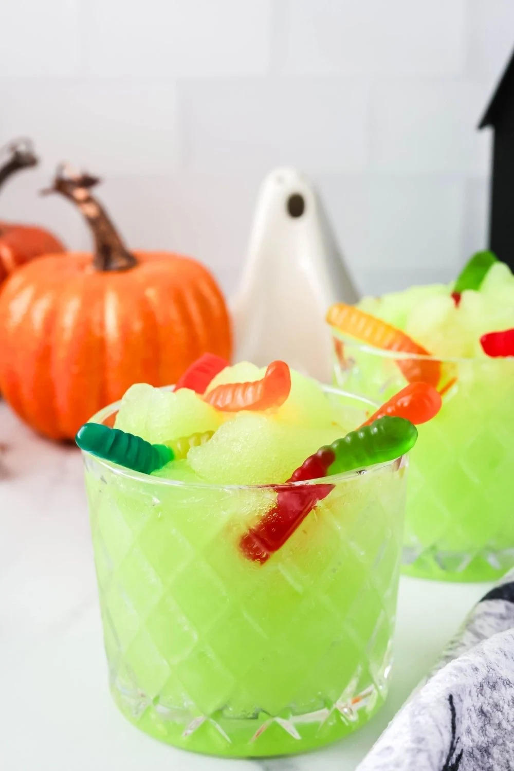 close-up of a glass of kid-friendly green Halloween slush made in the Ninja Slushi machine, garnished with colorful gummy worms.
