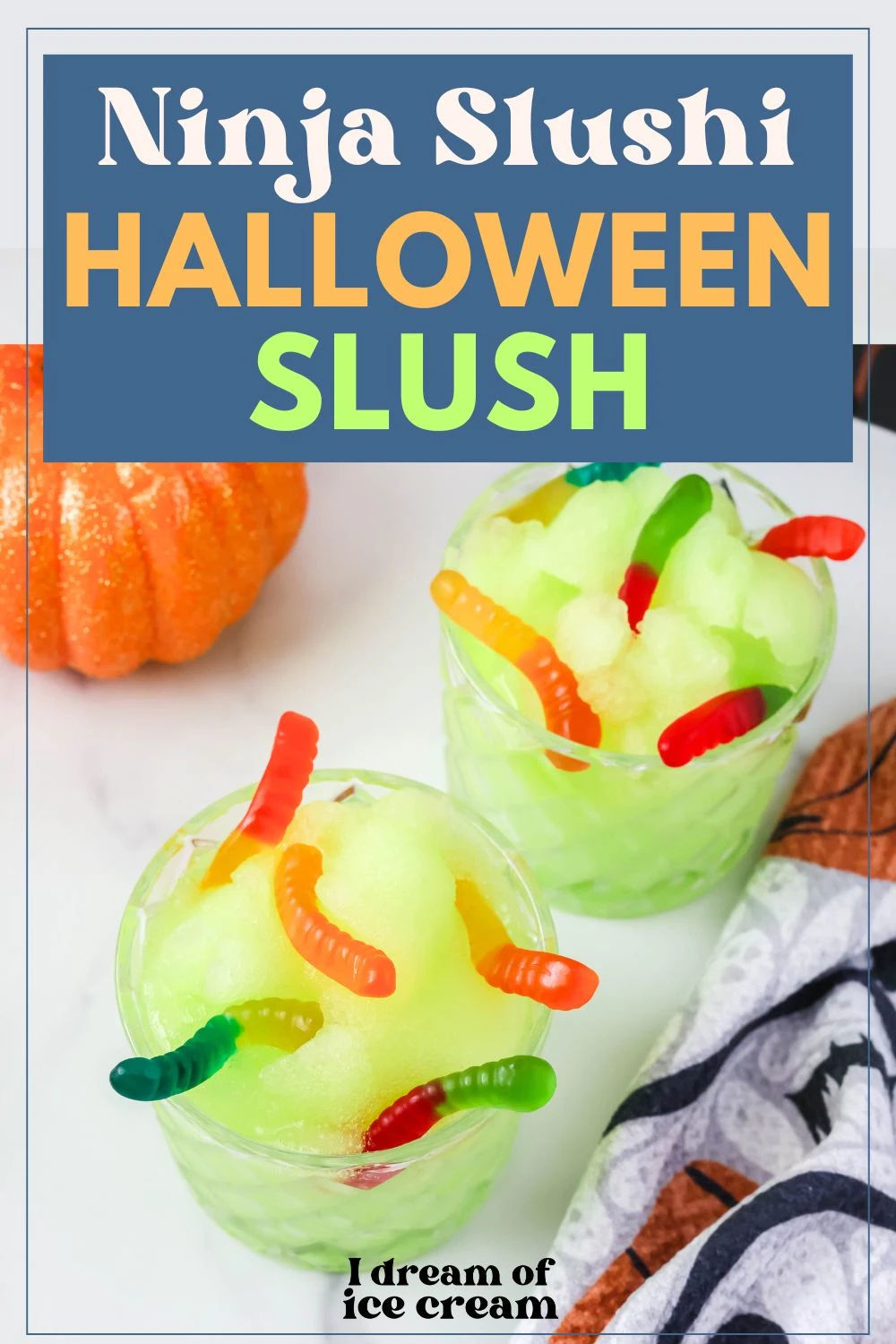 two glasses of Ninja Slushi witches' brew slush, garnished with gummy worms, next to a decorative pumpkin and Halloween kitchen towel.