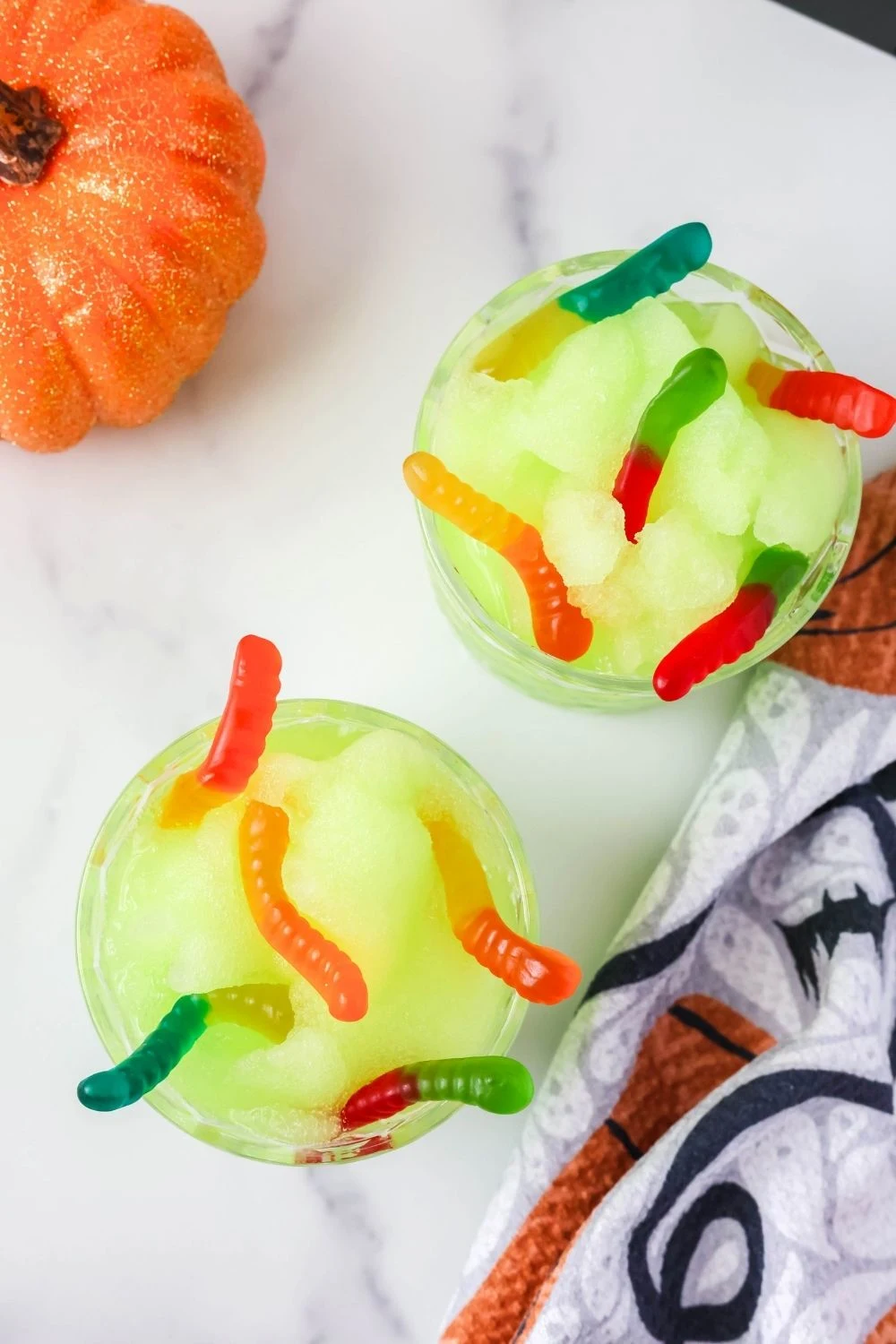 overhead view of two glasses of green nonalcoholic Ninja Slushi Halloween slush, topped with gummy worms.