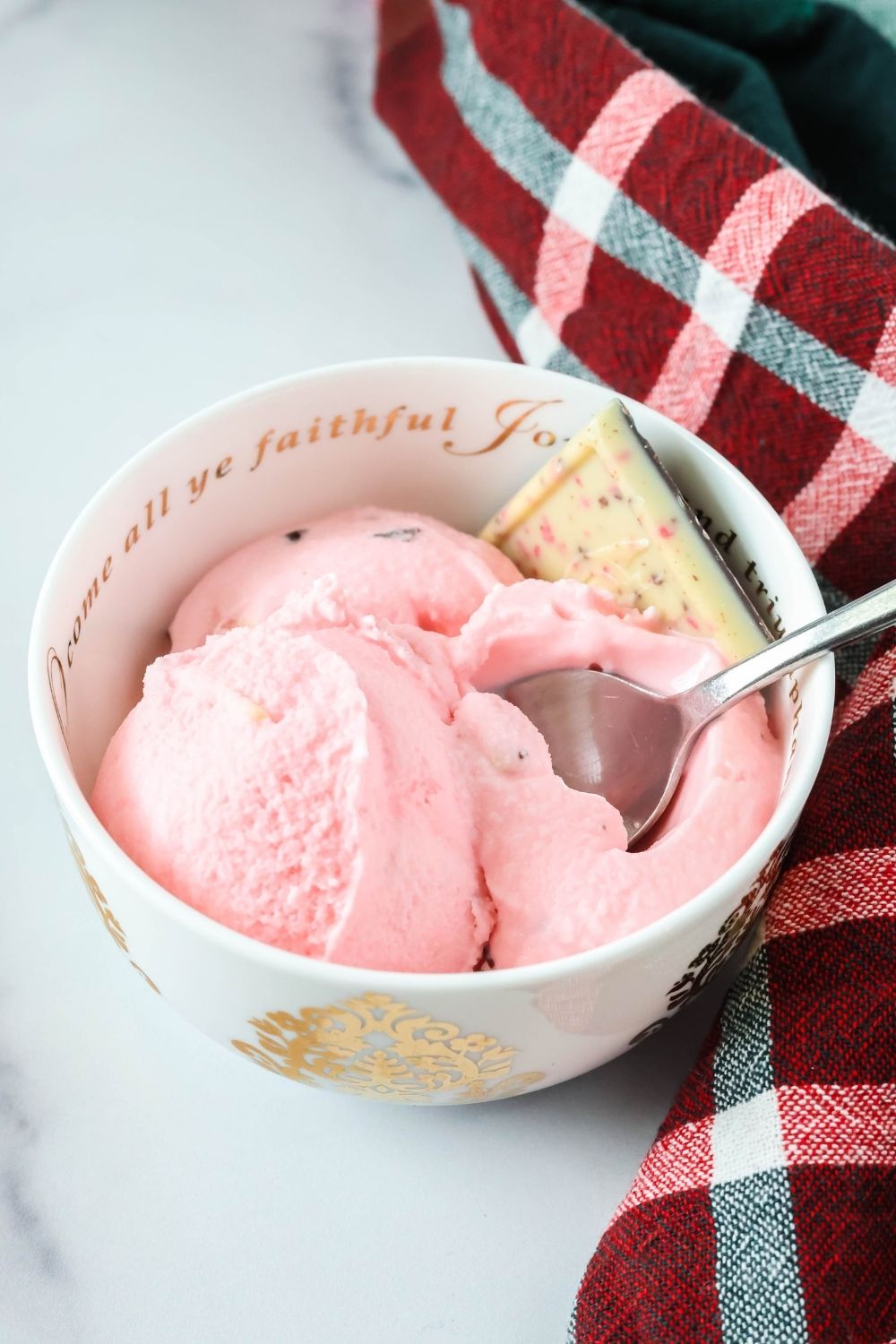 a white and gold bowl serves scoops of Christmas peppermint bark ice cream. A spoon is in the bowl.