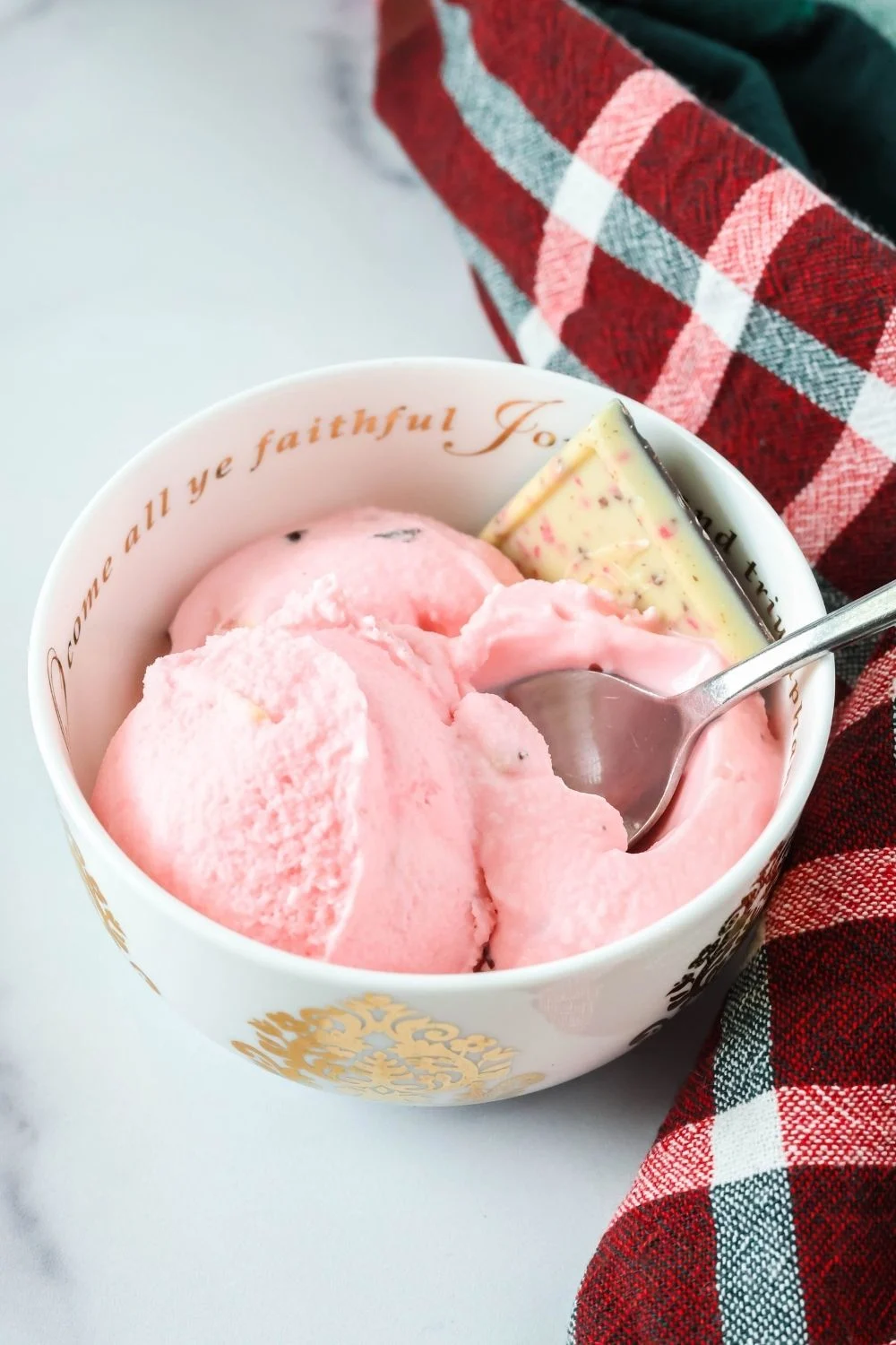 a white and gold bowl serves scoops of Christmas peppermint bark ice cream. A spoon is in the bowl.