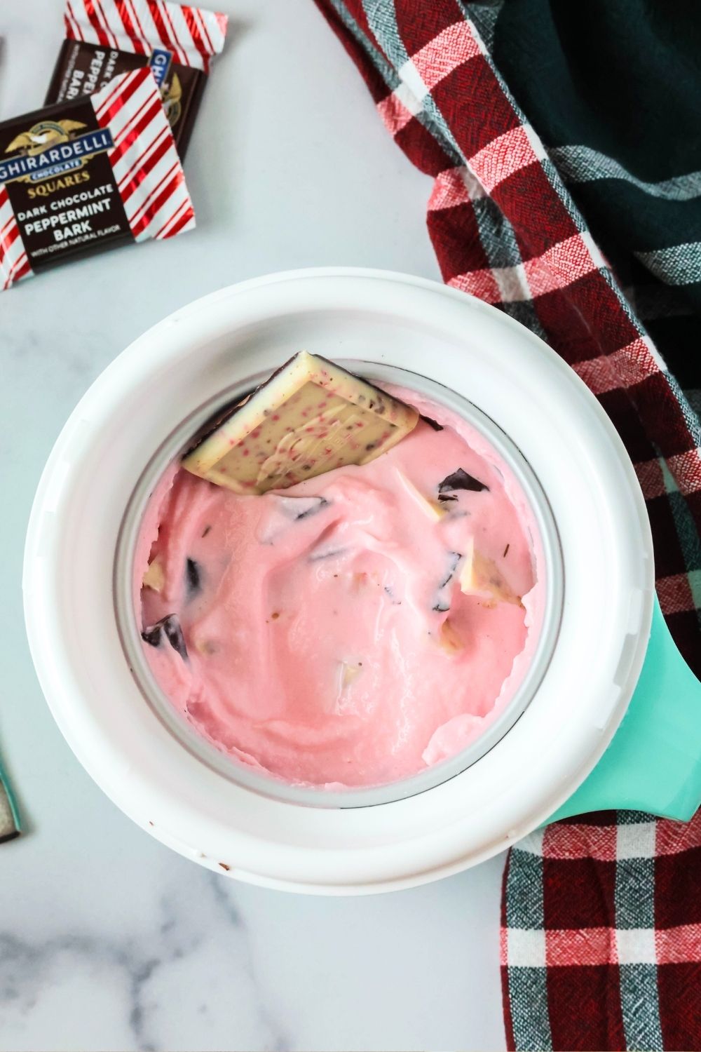 overhead view of a Dash Mug of peppermint bark ice cream. Squares of Ghirardelli peppermint bark are around the bowl.