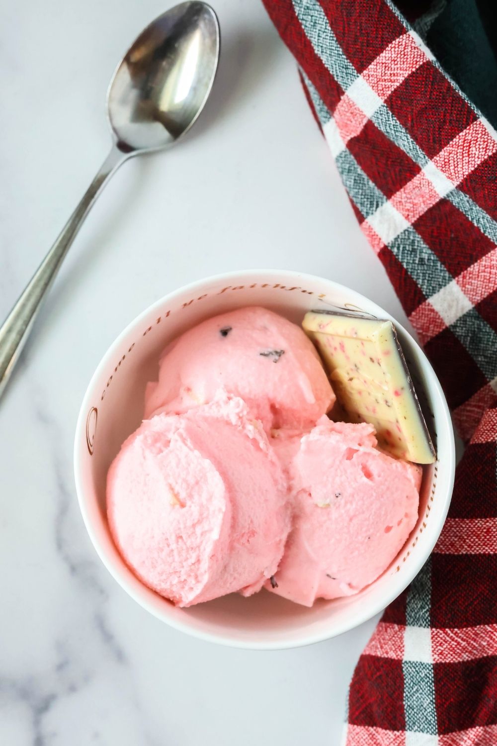 overhead view of a white bowl of peppermint bark ice cream for the holidays. A spoon is next to the bowl.