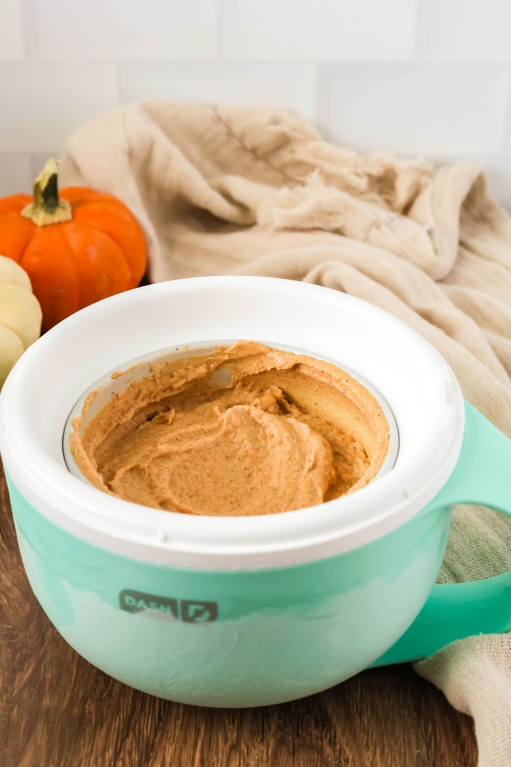 pumpkin spice ice cream in Dash My Mug ice cream maker. Two pumpkins are in the background.