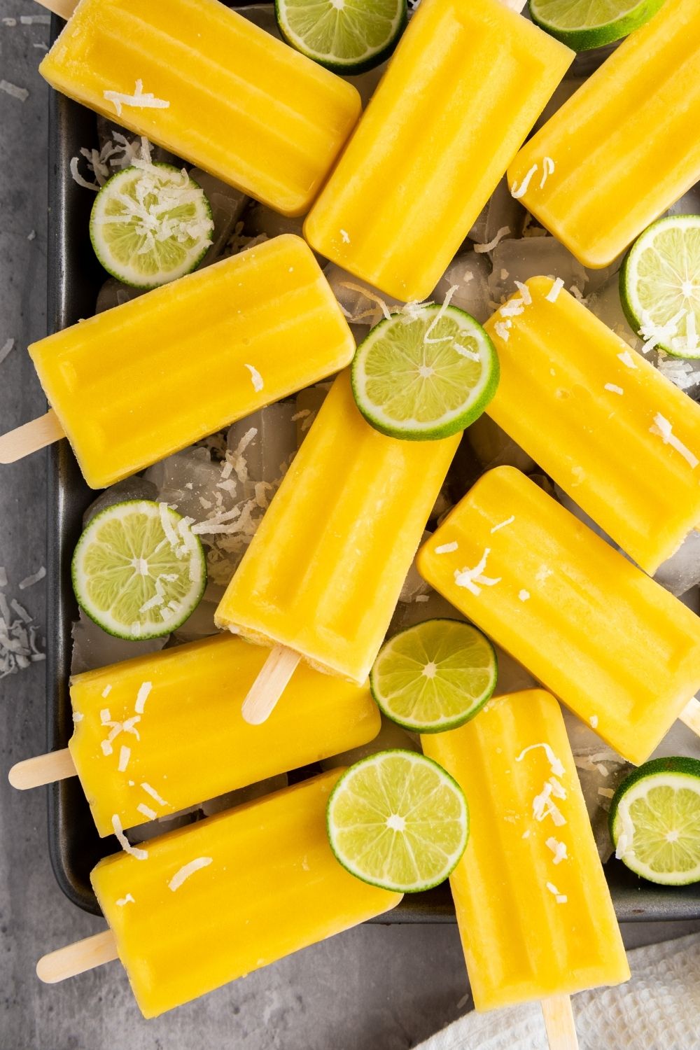 Creamy mango paletas on a tray with sliced limes.