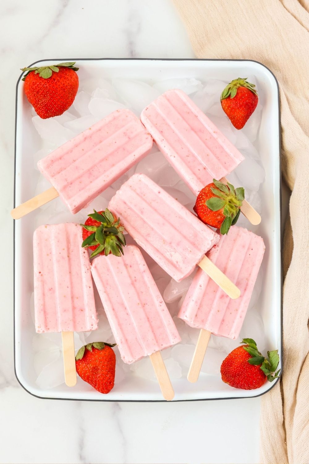 overhead view of a white tray of fresh strawberry yogurt pops, garnished with fresh strawberries.