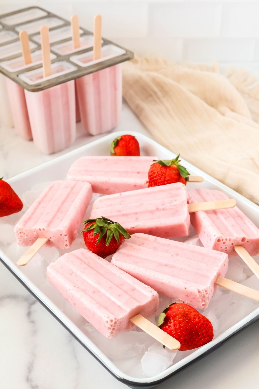 healthy strawberry popsicles on a white tray, with more popsicles in a popsicle mold in the background.