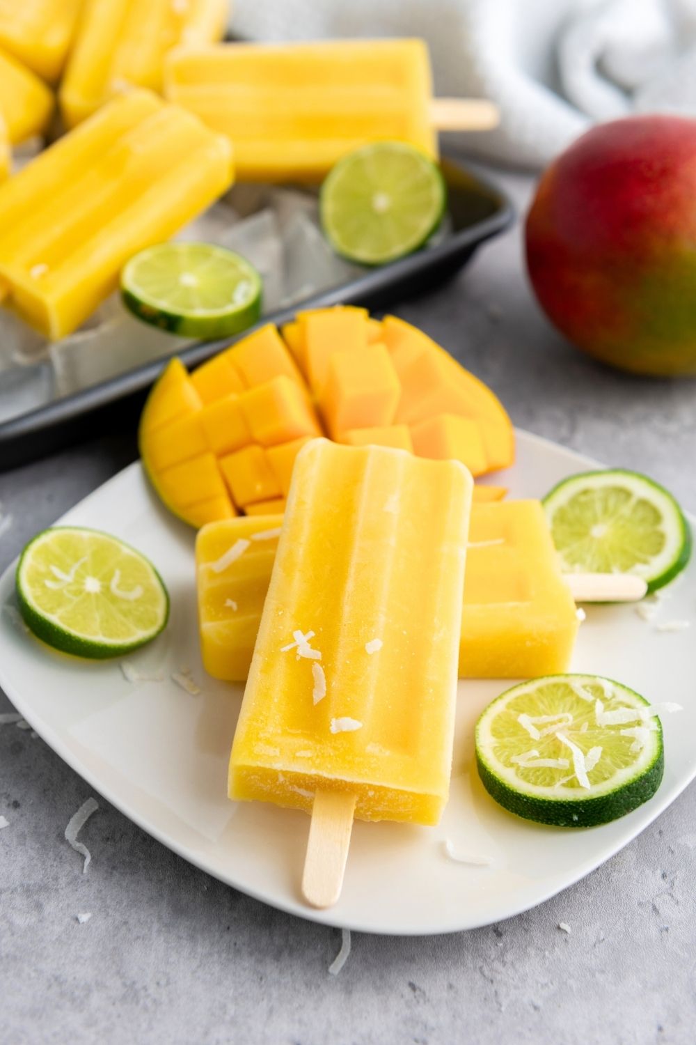 Homemade mango popsicles served on a white plate, garnished with lime slices.