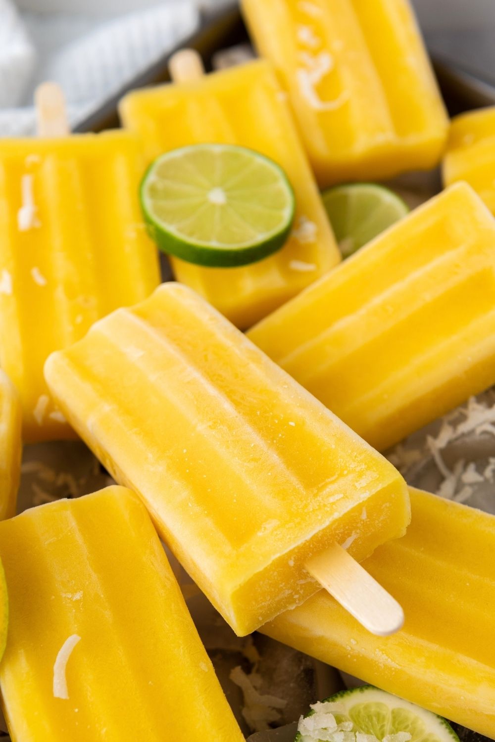 Mango lime yogurt pops stacked together with lime slices.