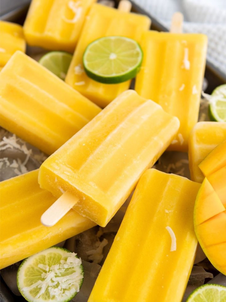 Homemade mango popsicles stacked together with slices of lime.