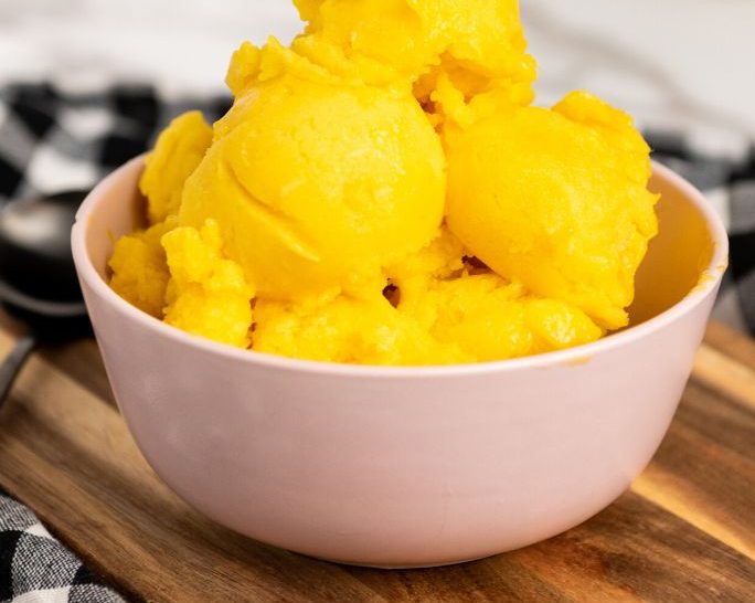 scoops of mango sorbet served in a light pink bowl.