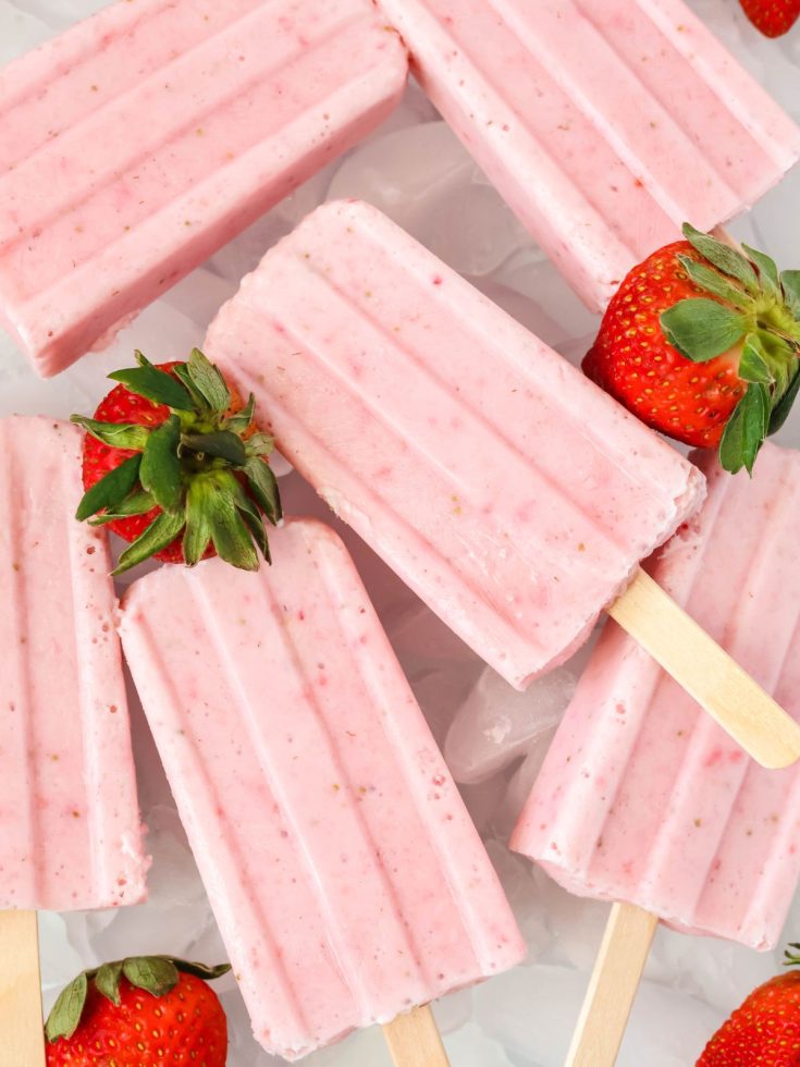 Strawberry Greek yogurt popsicles stacked together on a white serving tray along with fresh strawberries.