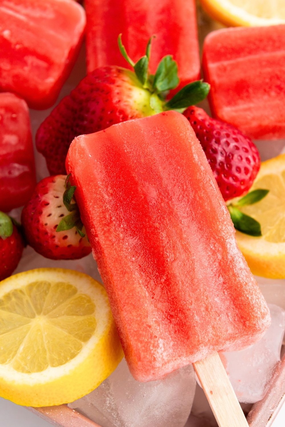 close-up view of a strawberry lemon popsicle, with fresh strawberries and sliced lemons next to it.