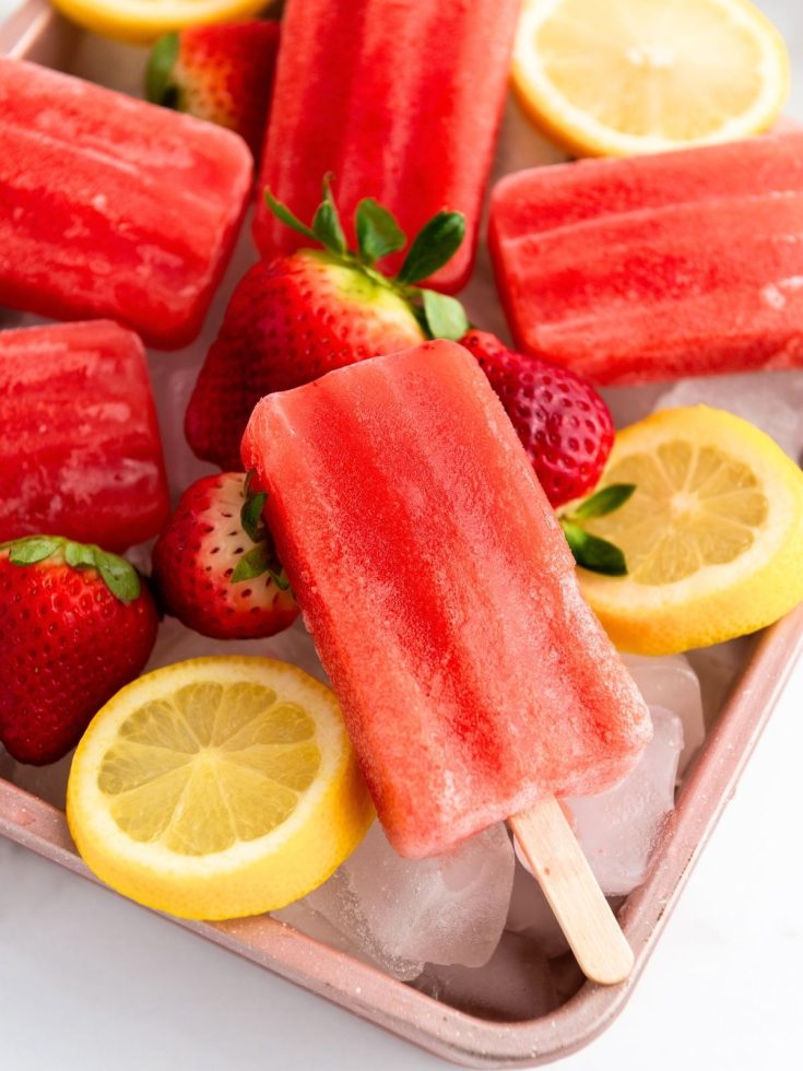 Homemade strawberry lemon popsicles served on a try, garnished with fresh strawberries and sliced lemons.
