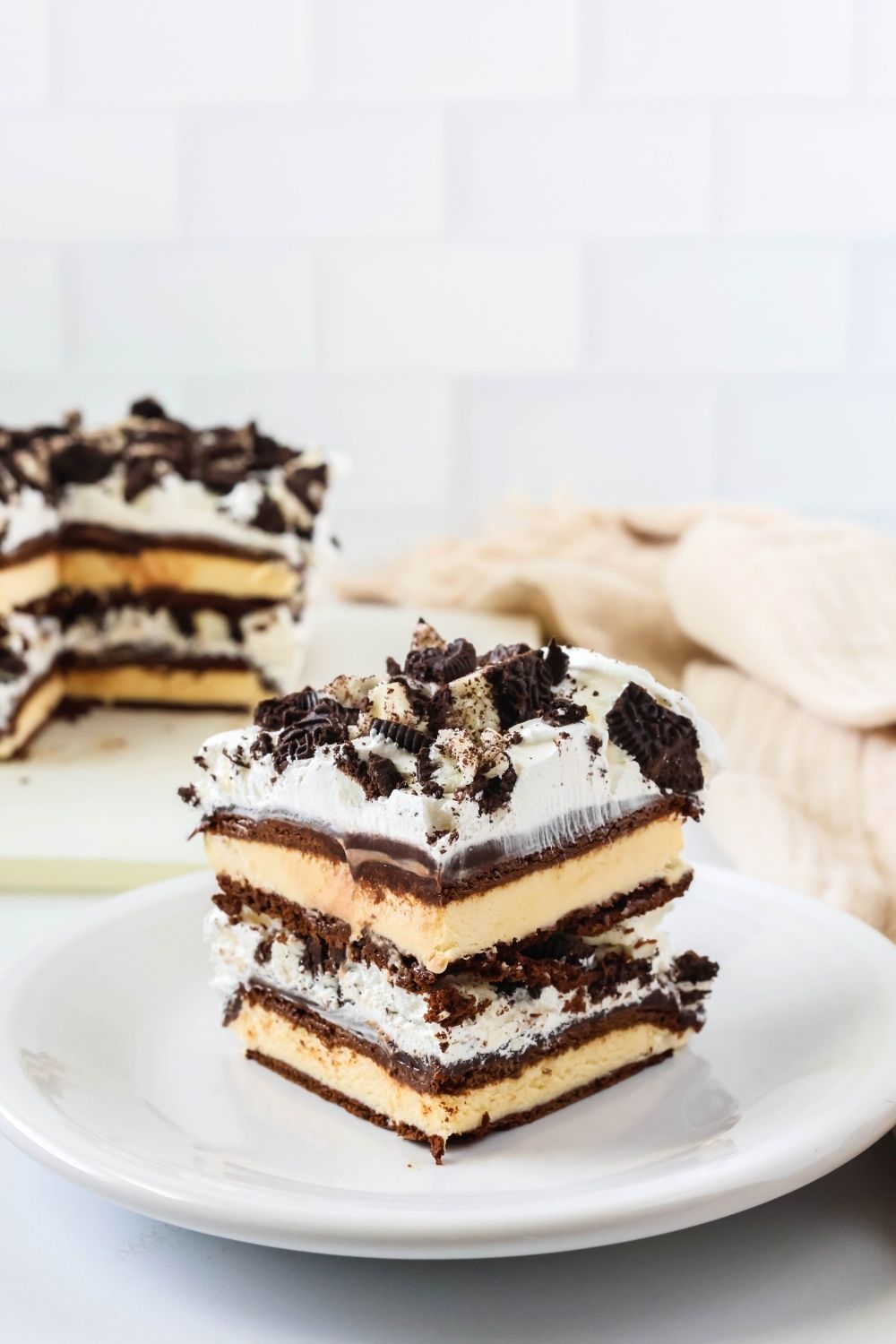 a slice of ice cream sandwich cake on a white plate, with the remainder of the ice cream cake in the background.