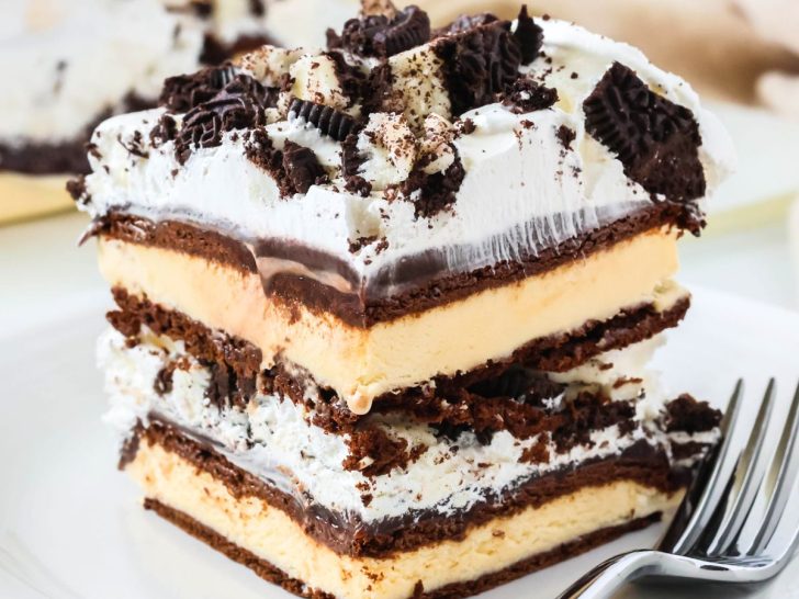 Slice of ice cream sandwich cake, made with hot fudge, Cool Whip, and Oreos, served on a white plate, with a fork next to it.