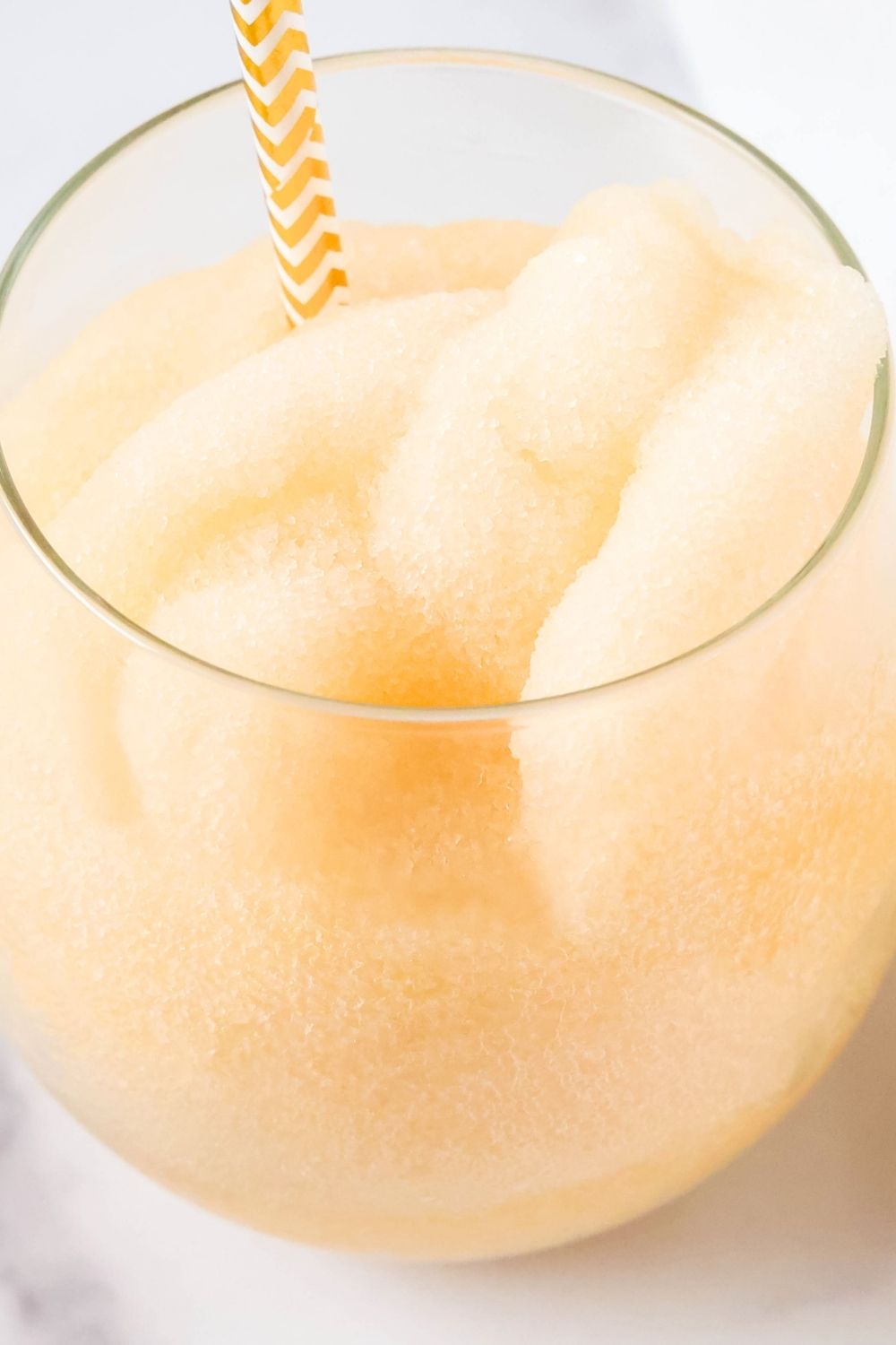 Ninja Slushi fizzy peach slush served in a wine glass with a gold and white patterned straw.