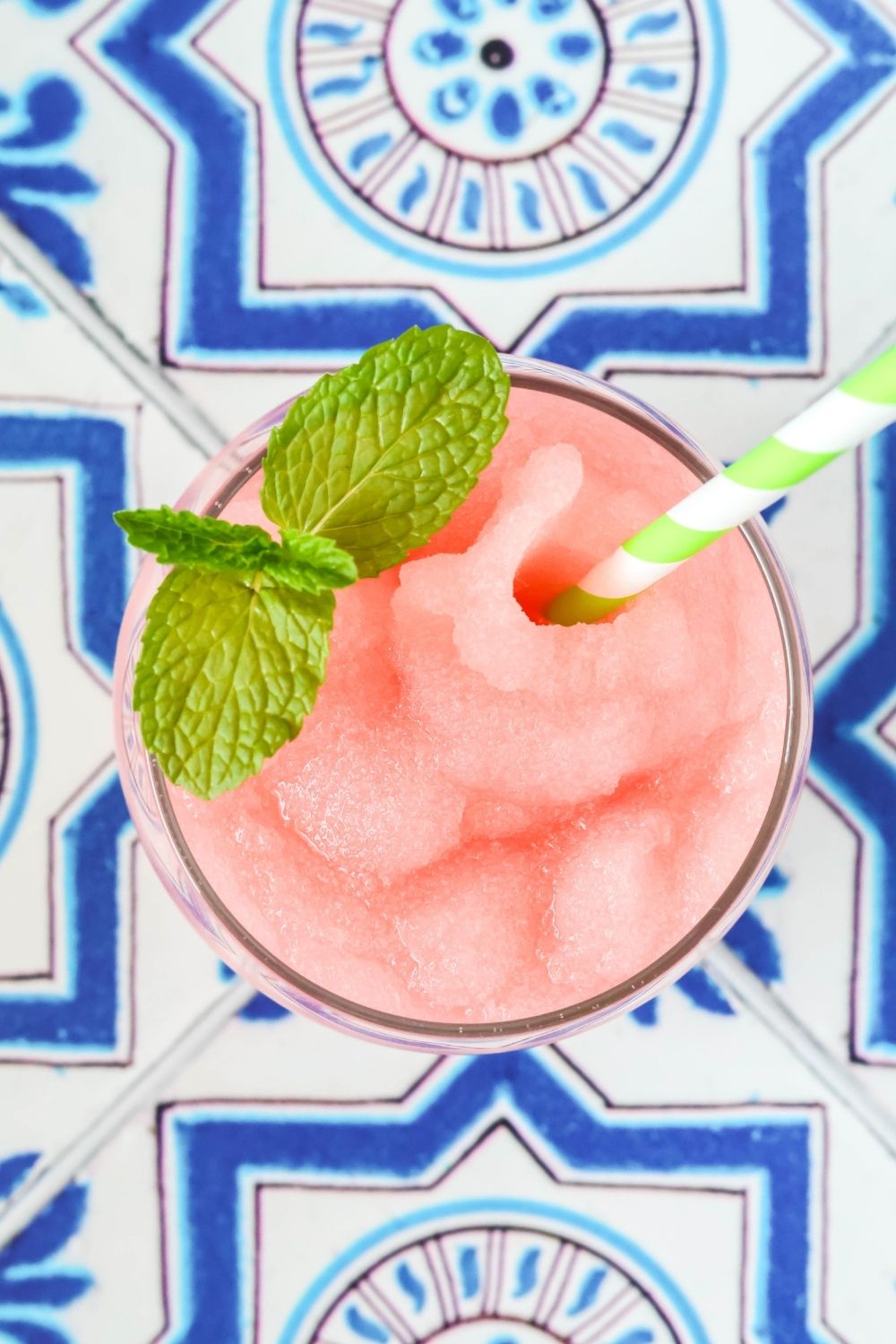 overhead view of a glass of limeade watermelon slush in a glass, garnished with fresh mint leaves. A green and white straw is in the glass.