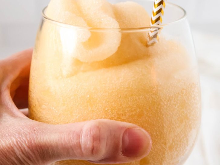 Ninja Slushi peach fizz slush in a glass, held by a woman's hand.