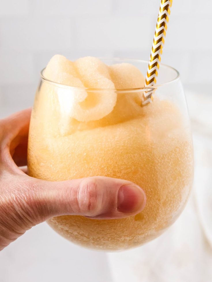 Ninja Slushi peach fizz slush in a glass, held by a woman's hand.