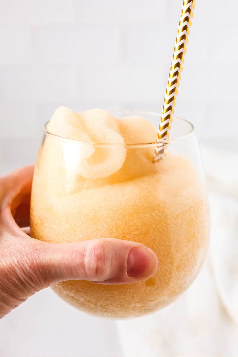 a woman's hand holds a stemless wine glass filled with peach ginger ale slushie made in the Ninja Slushi machine.