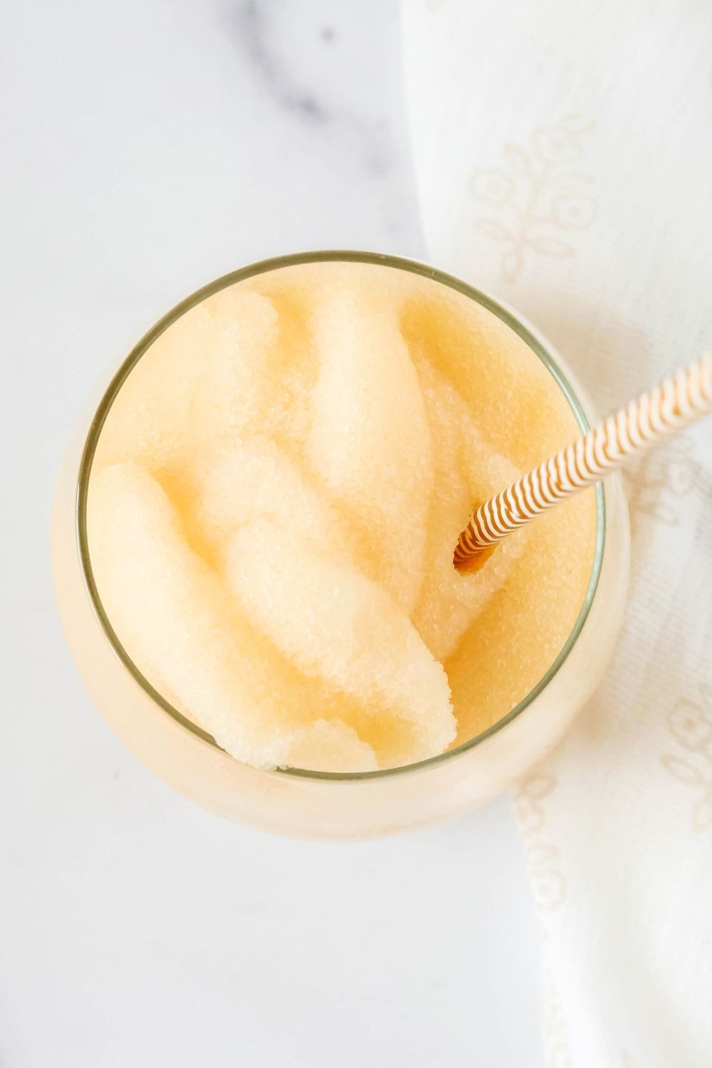 overhead view of a glass filled with peach slushie. A gold and white straw is in the glass.