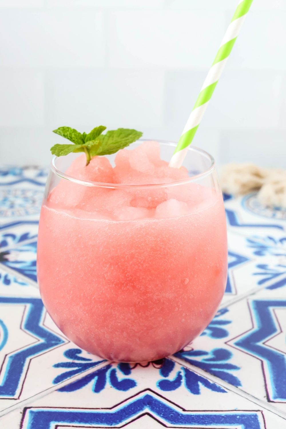 glass of watermelon limeade slushy made, garnished with mint leaves. A striped straw is in the glass.