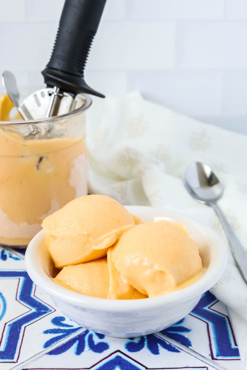 a white bowl of apricot sorbet, with a Ninja Creami pint container of sorbet in the background.