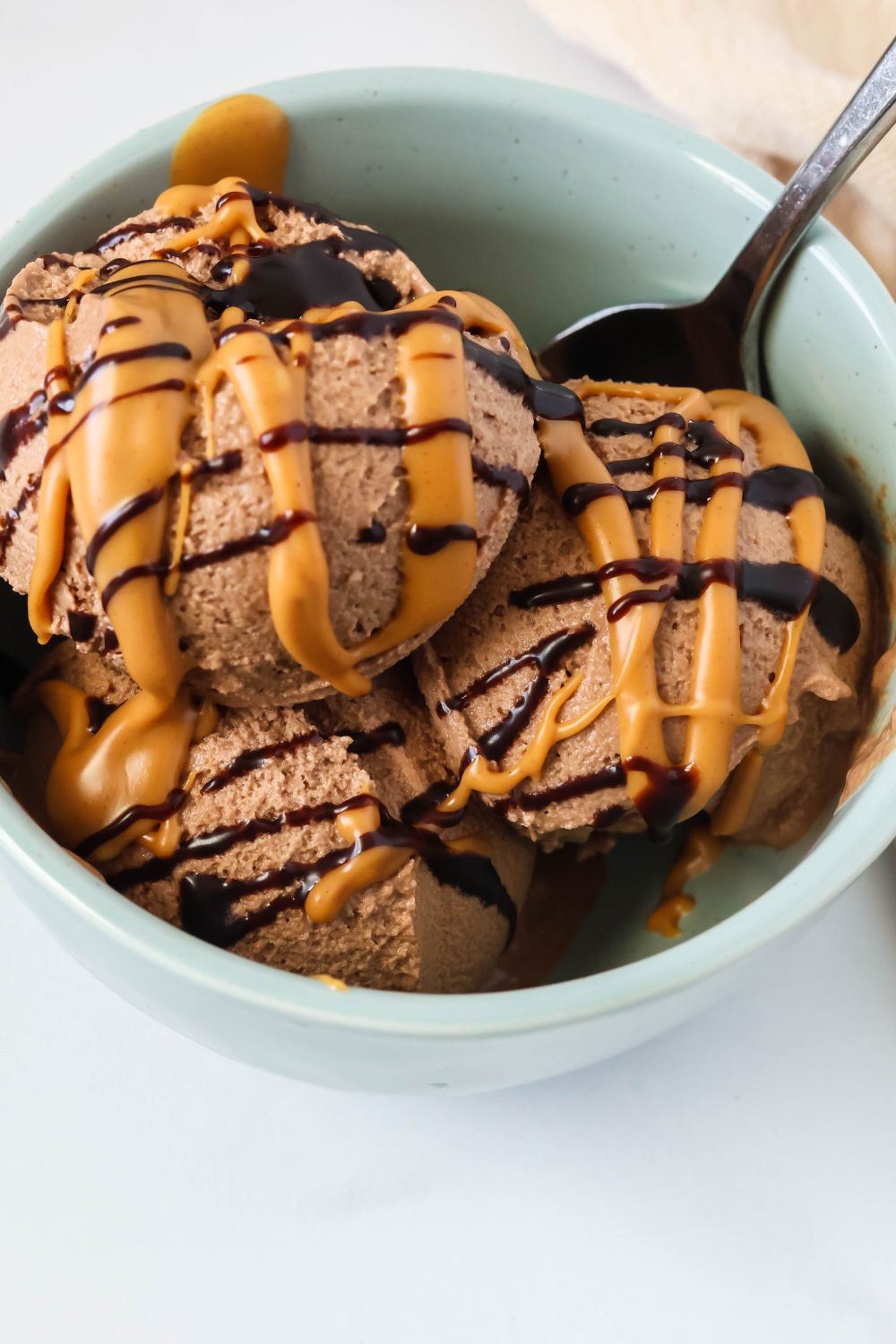 Close-up view of scoops of chocolate peanut butter ice cream in a blue bowl, drizzled with chocolate sauce and melted peanut butter.