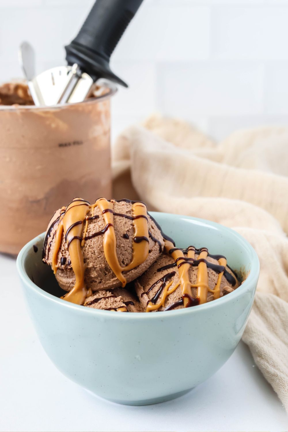 Bowl of Ninja Creami chocolate and peanut butter ice cream, with a pint of ice cream in the background.