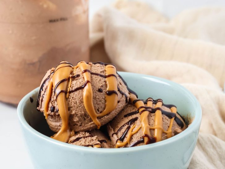 Scoops of Ninja Creami chocolate peanut butter ice cream in a blue bowl, topped with a peanut butter and chocolate drizzle. The Ninja Creami pint container is in the background.
