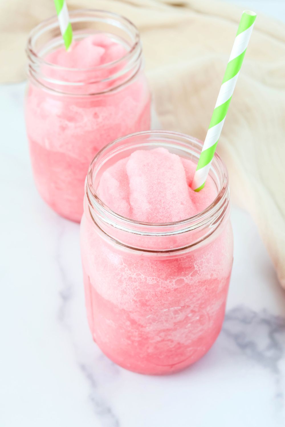 hibiscus lime slush served in two Mason jar glasses. Each glass has a lime green and white stripe straw in it.