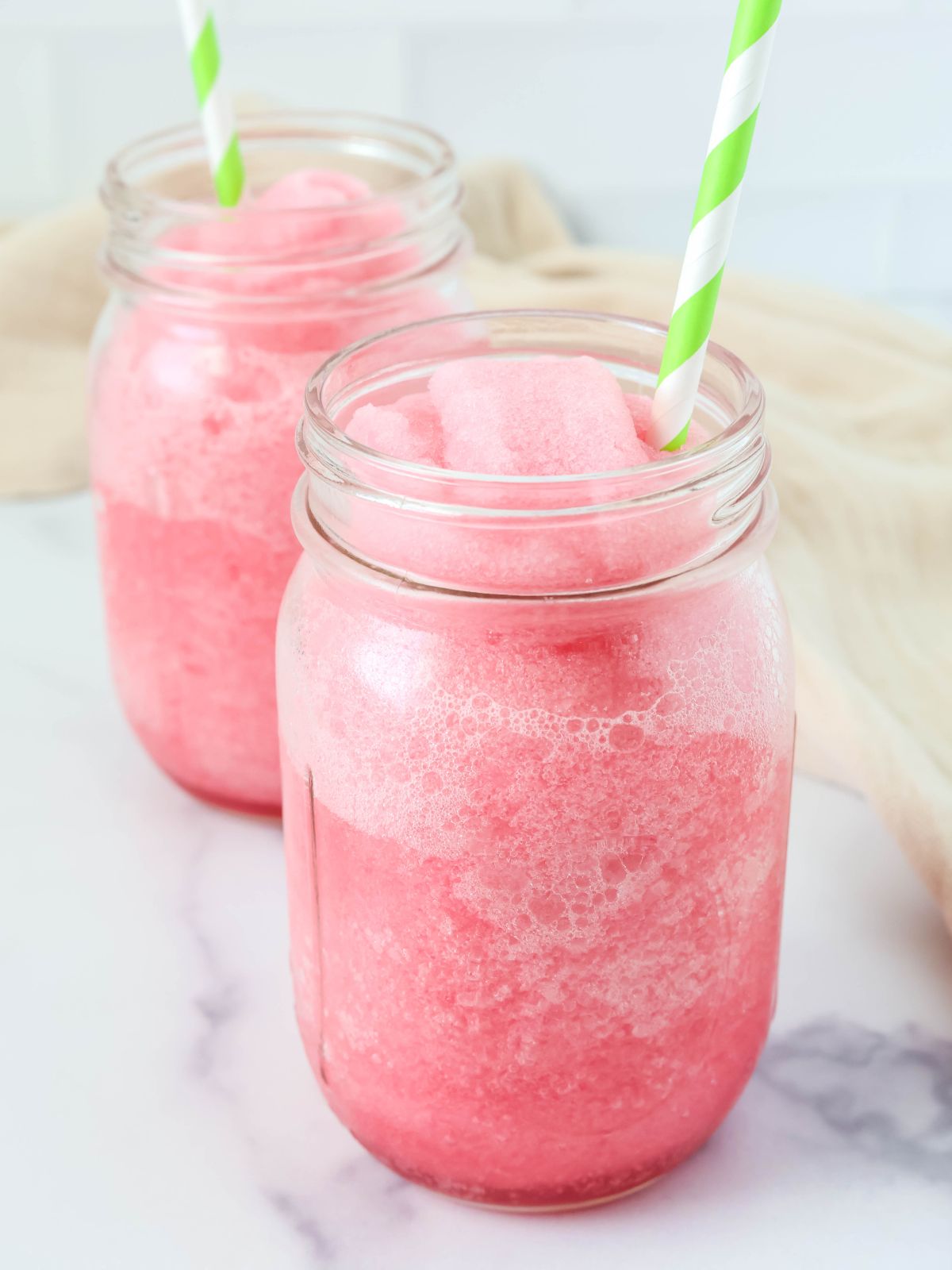 Ninja Slushi hibiscus limeade served in two Mason jar glasses with green and white straws.
