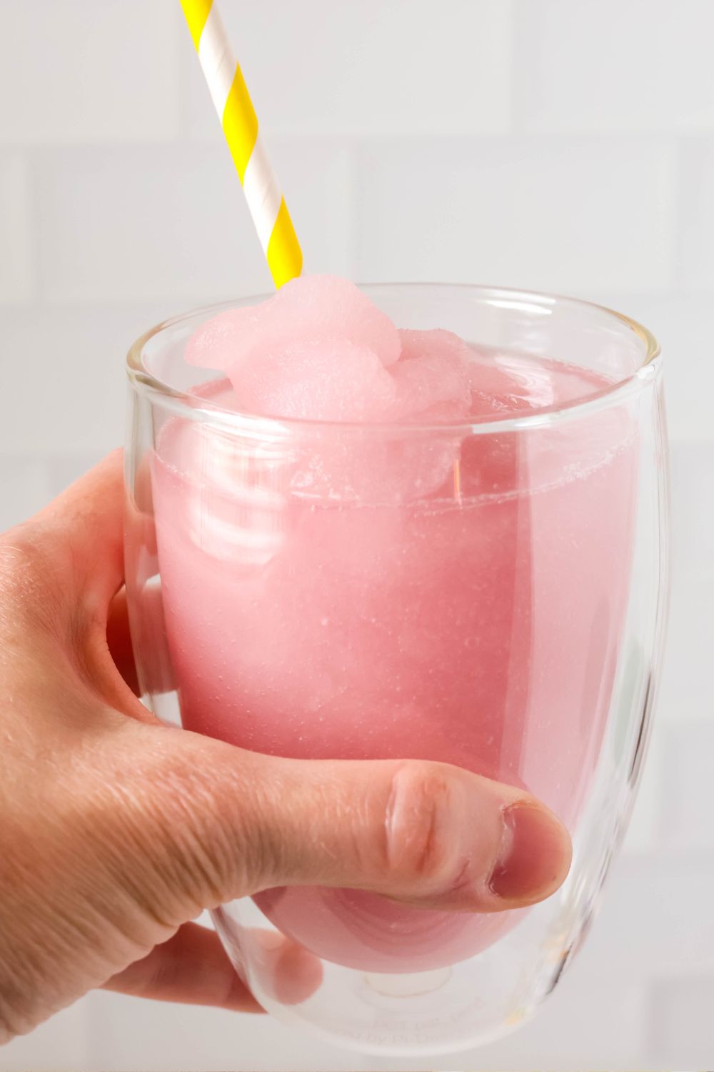 A woman's hand holds a glass of copycat Epcot violet lemonade slush with a yellow striped straw in it.