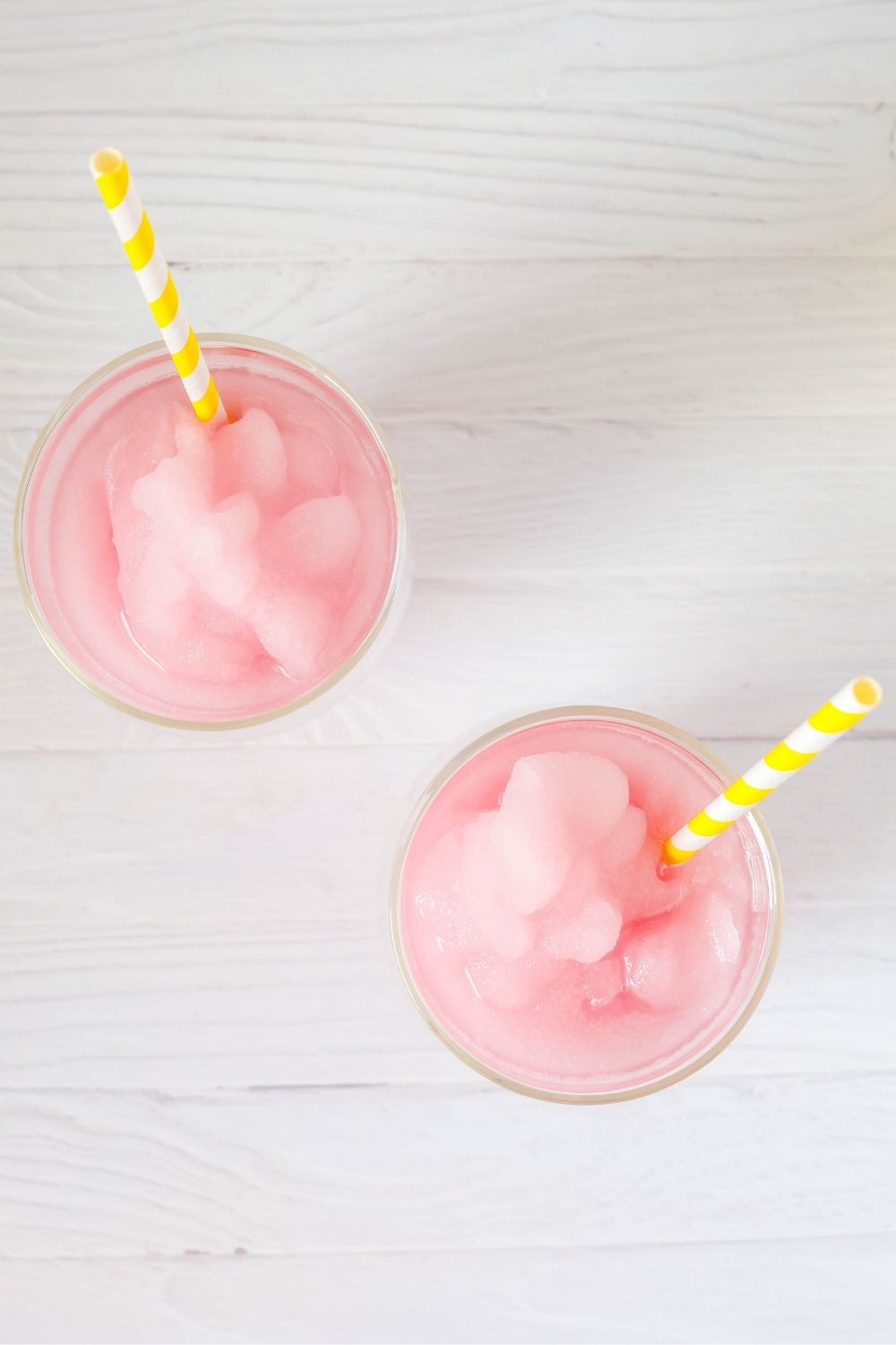 overhead view of two glasses filled with violet lemonade slush. The glasses each have a yellow and white stripe straw in it.